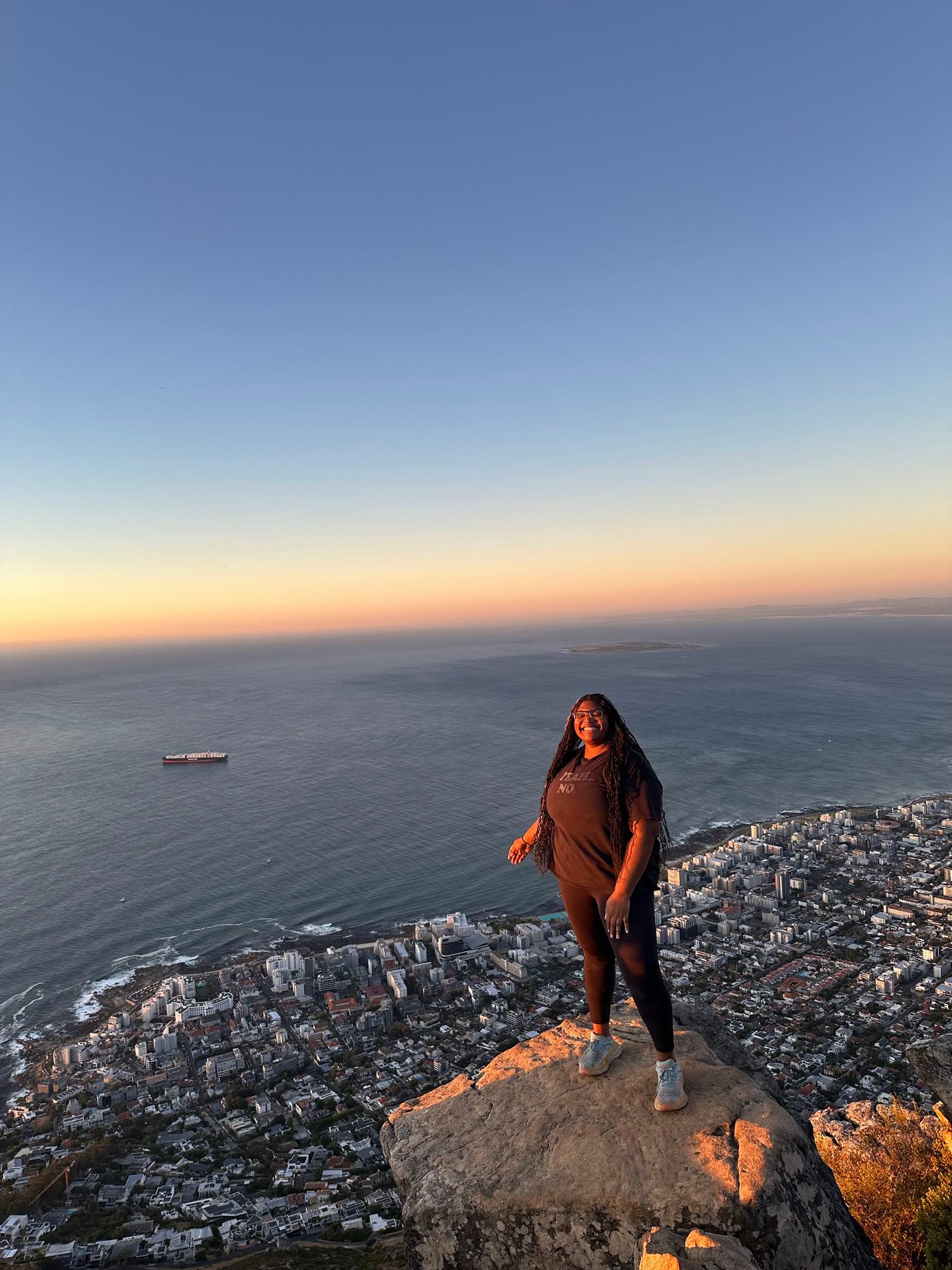 Standing on a rocky summit above Cape Town at sunset, with the Atlantic and the city spread out below.